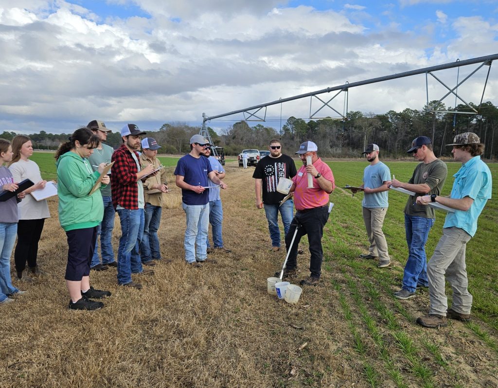 A dozen people are standing in an agricultural field.