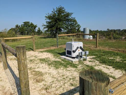 White and gray cube with handles on a cement pad inside a fenced pen.