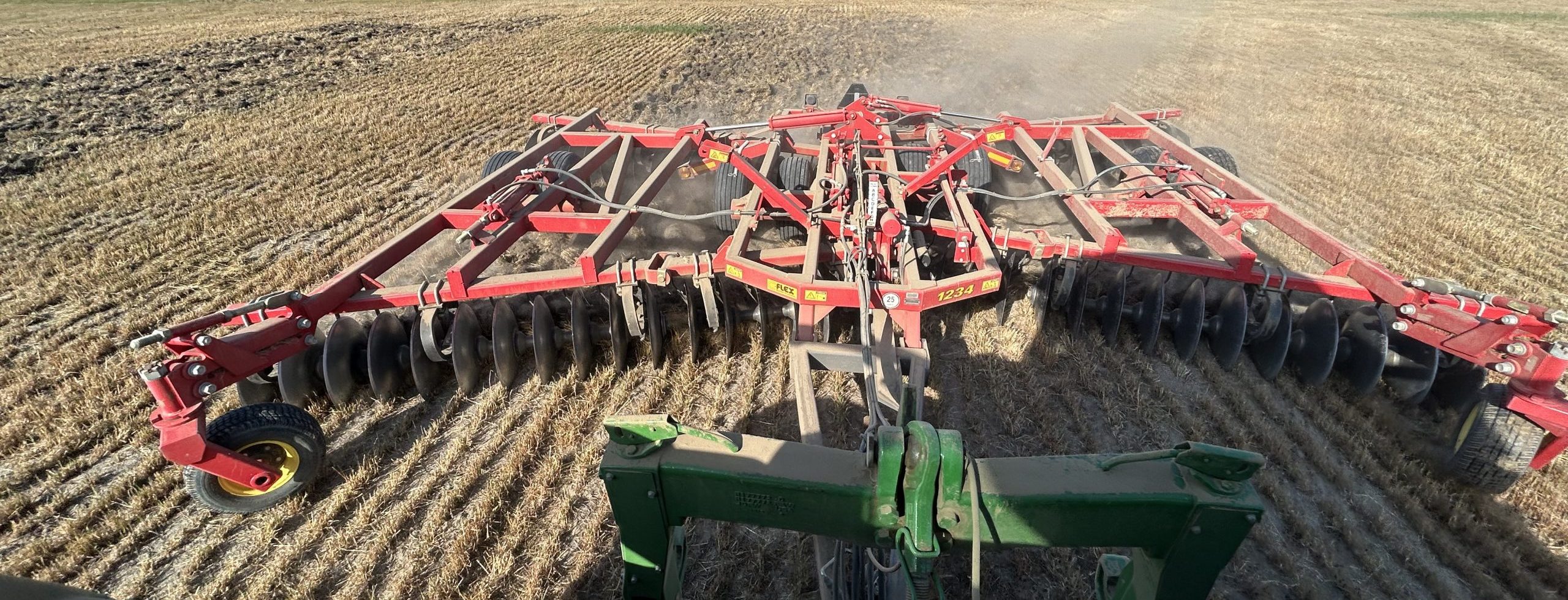 Photo of a Sunflower disk, which is a tractor attachment with many circular blades, being run through a field of dry plant residue.