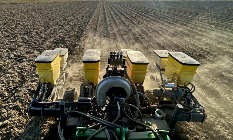 Planter being pulled behind a tractor, planting peanut seeds in an agricultural field.