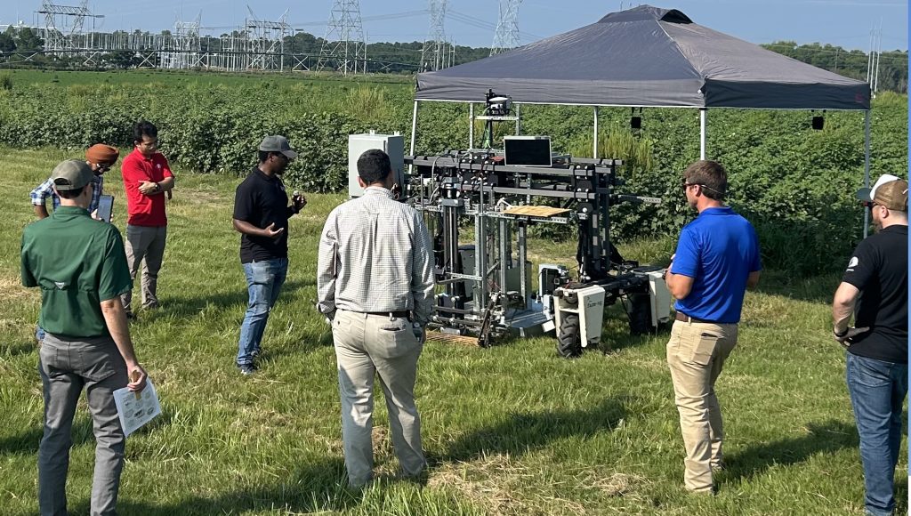 People grouped around a black tent-topper, talking about a gray robotic machine.